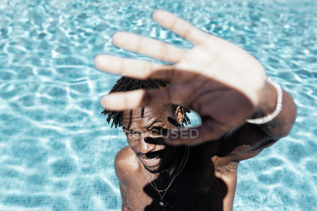 From above of African American male with naked tors standing in pool and covering face from sun while looking at camera — Stock Photo