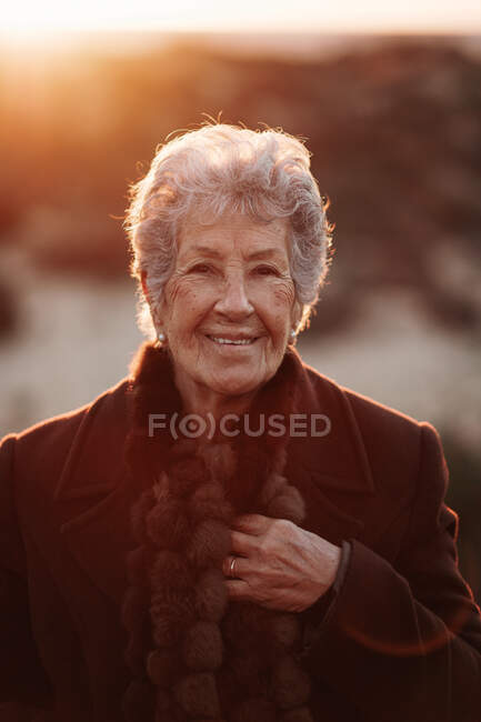 Viandante anziana in abiti casual in piedi su un molo di legno sulla spiaggia di sabbia e godersi il paesaggio marino al tramonto — Foto stock