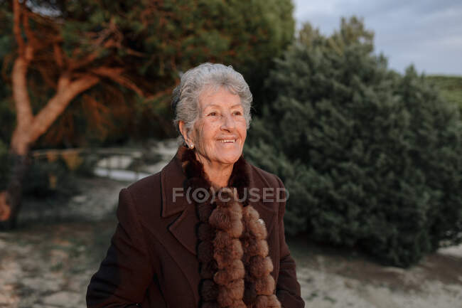 Viandante anziana in abiti casual in piedi su un molo di legno sulla spiaggia di sabbia e godendo paesaggio marino e guardando altrove — Foto stock