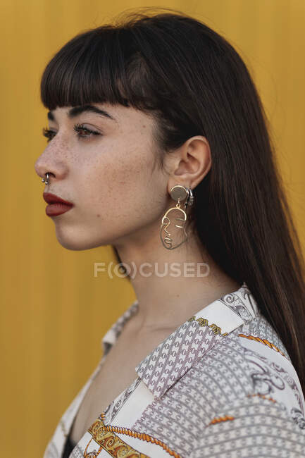 Side view of gorgeous confident young ethnic woman with ling dark hair in casual clothes and stylish earrings standing on street and looking away thoughtfully — Stock Photo