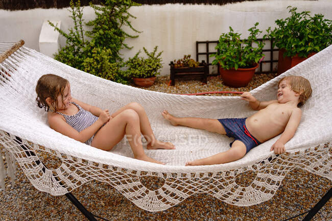 Cute barefooted little sister and brother lying in hammock and having fun during summer holidays — Stock Photo