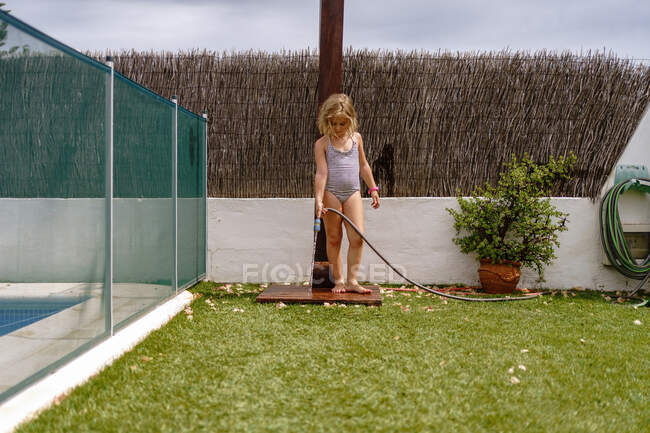 Carino bambina in costume da bagno a piedi e irrigazione prato verde dal tubo durante le vacanze estive in campagna — Foto stock
