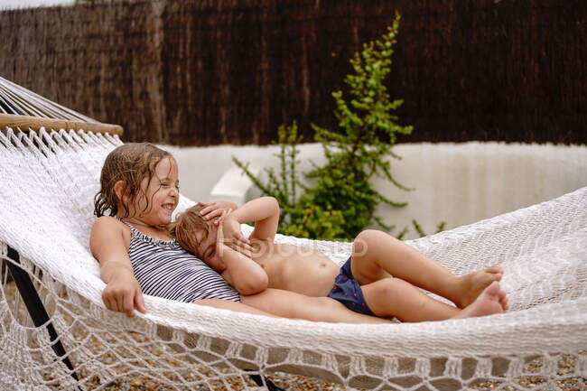 Bonito descalço irmãzinha e irmão abraçando enquanto deitado na rede e se divertindo durante as férias de verão — Fotografia de Stock