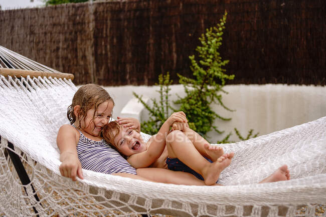 Carino a piedi nudi sorellina e fratello abbracciare mentre sdraiato in amaca e divertirsi durante le vacanze estive — Foto stock