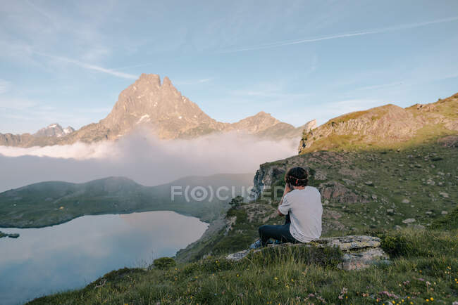 Dall'alto vista posteriore del turista maschio anonimo che scatta foto del monte nella nebbia sulla macchina fotografica sotto cielo nuvoloso — Foto stock