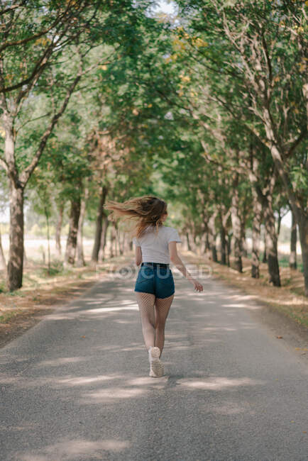 Back view of anonymous female jogger in sports clothes running on pathway between trees during workout in daytime — Stock Photo