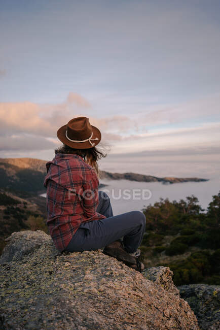 Vista posteriore di turista donna irriconoscibile in cappello ammirando l'oceano con orizzonte da montagna sotto cielo nuvoloso — Foto stock