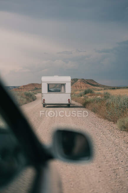 Através do espelho lateral do carro vista da estrada reta com caravana contra a paisagem rural da montanha — Fotografia de Stock