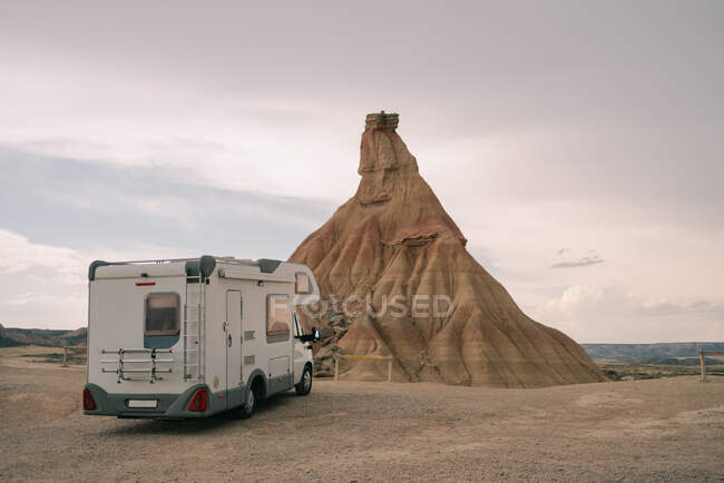 Motorhome припаркован на песчаной местности против скалы с ухабистой поверхностью под облачным небом в дневное время — стоковое фото