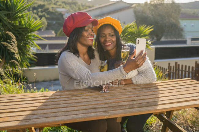 Дві чорні сестри-близнюки, сидячи на лавці, роблять селфі з мобільним телефоном. — стокове фото