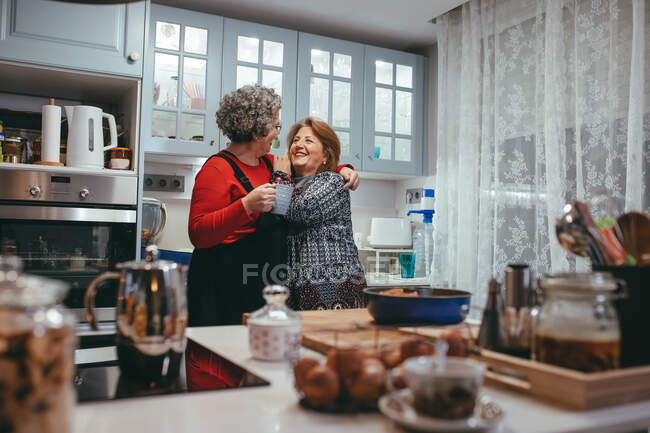 Contenidos homosexuales maduras parejas femeninas con taza de café abrazándose y mirándose en casa - foto de stock