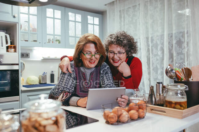 Lächelnde homosexuelle ältere Frauen, die während eines Videochats zu Hause ein Tablet anschauen — Stockfoto