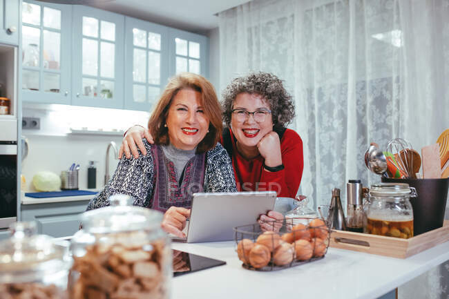 Sorrindo homossexual mulheres idosas assistindo tablet durante vídeo chat em casa olhando para a câmera — Fotografia de Stock
