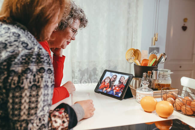 Side view of smiling homosexual elderly women watching tablet with happy children and mothers during video chat at home — Stock Photo