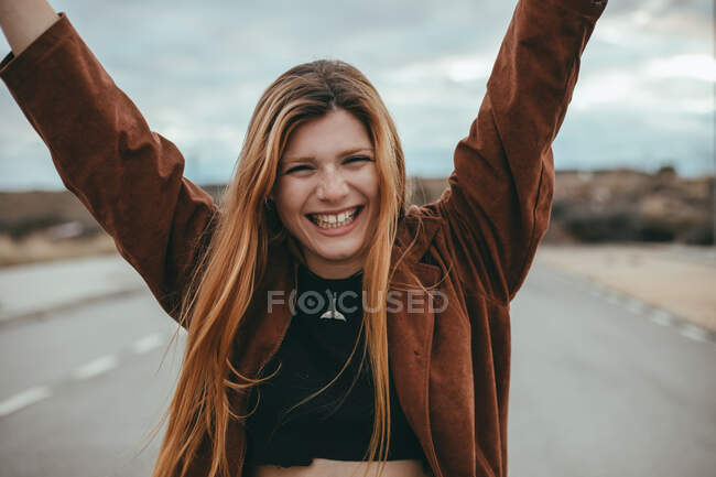 Fröhliche junge Frau mit langen Ingwerhaaren steht an bewölkten Tagen auf der Straße und blickt in die Kamera — Stockfoto