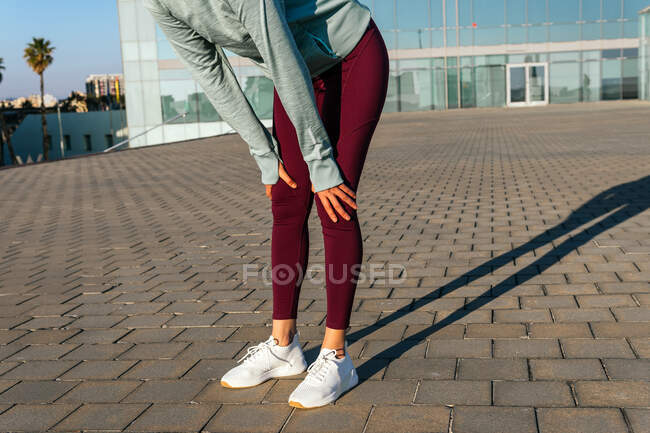 Crop female athlete in stylish sportswear standing near modern glass building on city street — Stock Photo