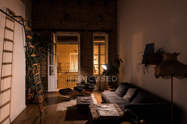 Interieur des Wohnzimmers mit grünen Topfpflanzen und bequemem Sofa in Wohnung im Loft-Stil in der Nacht — Stockfoto