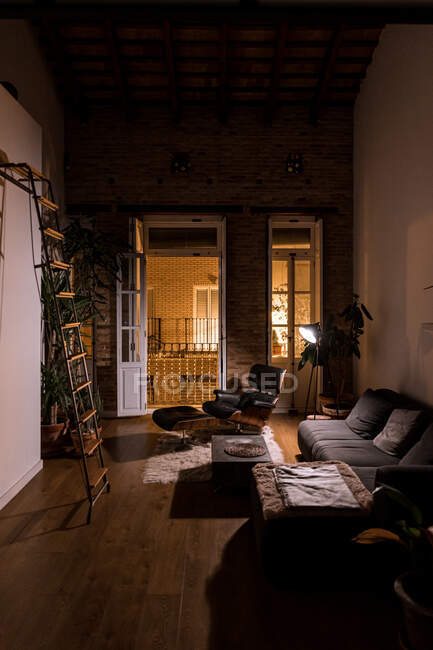 Interior da sala de estar com plantas envasadas verdes e sofá confortável no apartamento em estilo loft à noite — Fotografia de Stock