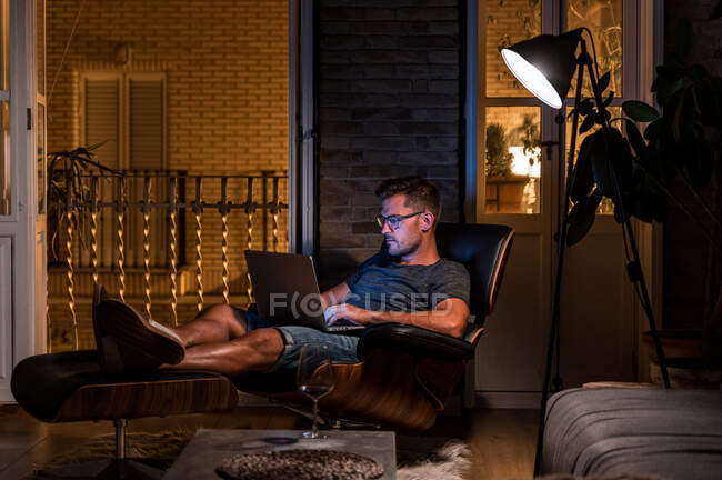 Занятый мужчина-предприниматель, сидящий в кресле и работающий над проектом, используя ноутбук и смартфон — стоковое фото