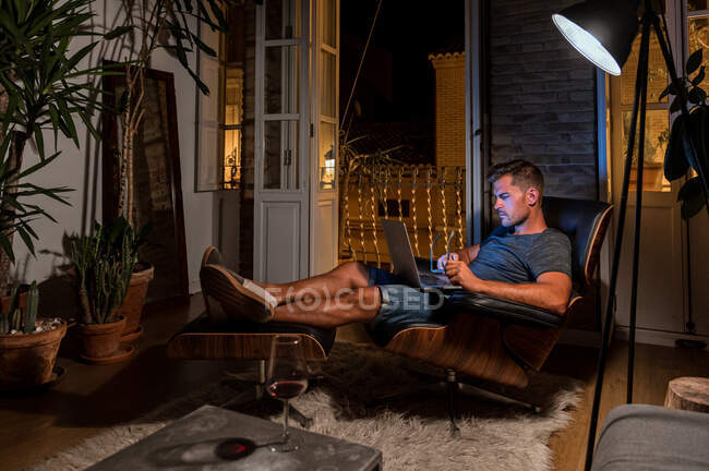 Empresario masculino ocupado sentado en sillón y trabajando en el proyecto mientras usa el ordenador portátil - foto de stock
