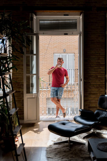 Homme détendu en tenue domestique debout sur le balcon et dégustant du vin blanc frais — Photo de stock