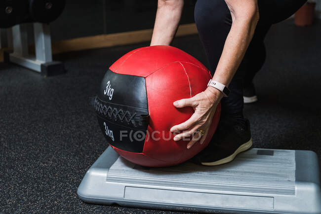 Анонімна старша жінка-спортсменка в спортивному одязі, що спирається вперед, приймаючи медичний м'яч під час тренувань у гімназії — стокове фото