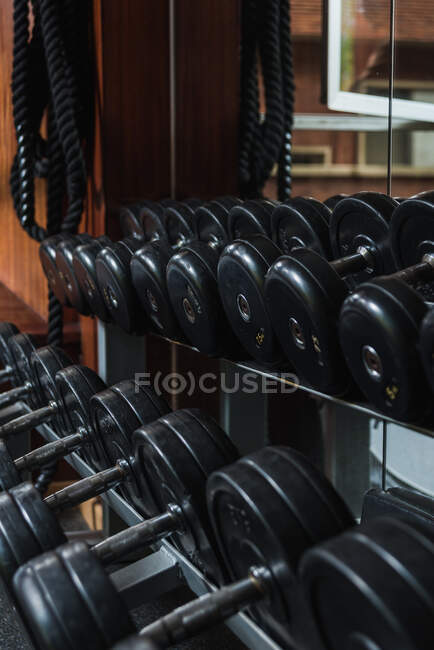 Schwere schwarze Hanteln mit Metallstangen und -platten, die sich tagsüber im Spiegel in der Sporthalle spiegeln — Stockfoto