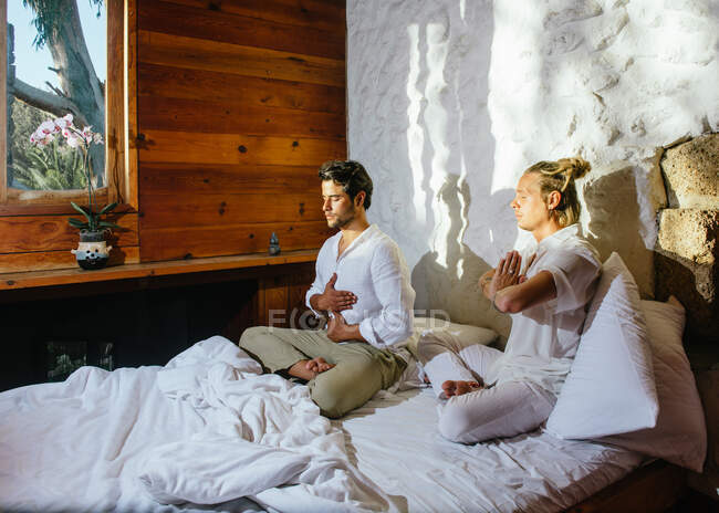 Dos amigos sentados en una cama mientras practican meditación - foto de stock