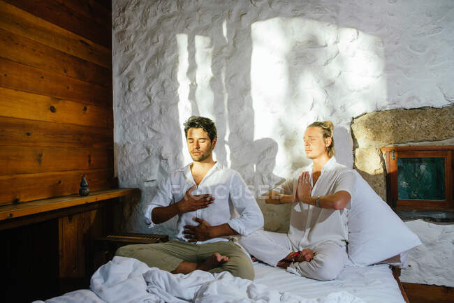 Dos amigos sentados en una cama mientras practican meditación - foto de stock