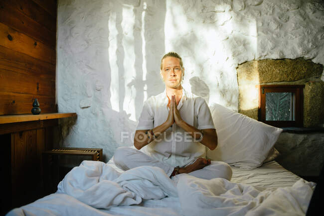 Blonder Mann sitzt auf einem Bett und übt Meditation — Stockfoto