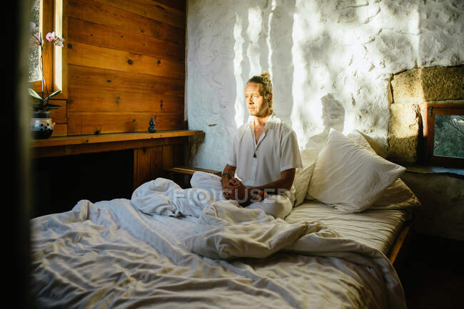 Blonder Mann sitzt auf einem Bett und übt Meditation — Stockfoto