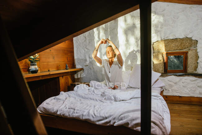 Hombre rubio sentado en una cama mientras practica meditación - foto de stock