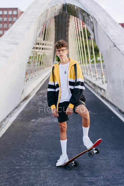 Adolescente caucásica de pie con un monopatín en el medio del puente en la ciudad - foto de stock