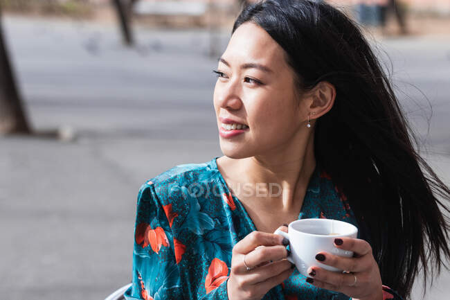 Long-haired brunette Asian woman having a coffee on a terrace of a cafe — Stock Photo