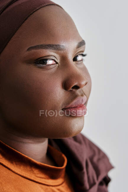 Portrait de séduisante jeune femme noire en vêtements décontractés et turban regardant la caméra — Photo de stock