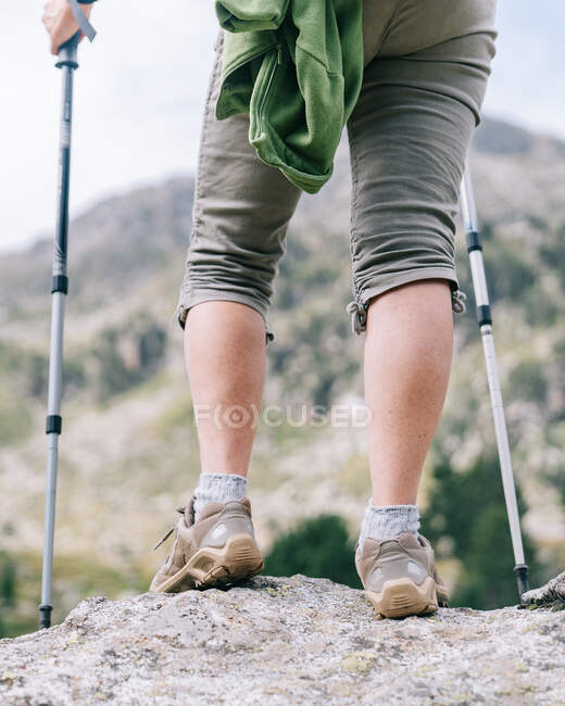 Обрезанная анонимная женщина-туристка в повседневной одежде с рюкзаком с палками для прогулок, стоя на каменистой вершине холма в горной долине Руда в Пиренеях Каталонии — стоковое фото