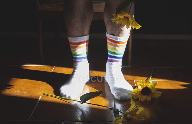 Crop mâle anonyme avec fleur fraîche en fleurs portant des chaussettes avec des rayures arc-en-ciel à la lumière du soleil — Photo de stock