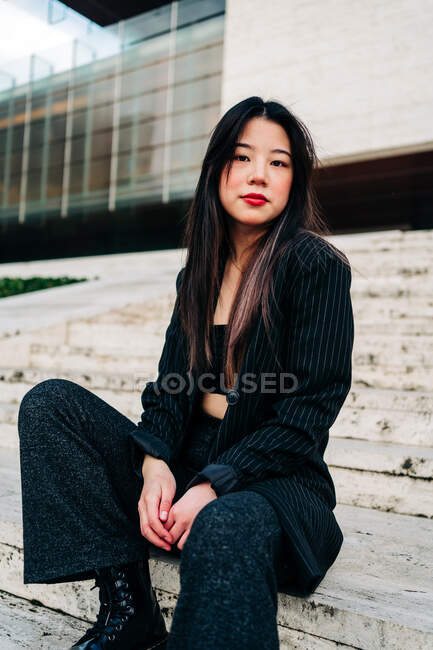 Довге волосся брюнетка азіатська жінка сидить на деяких сходах і дивиться на камеру — стокове фото