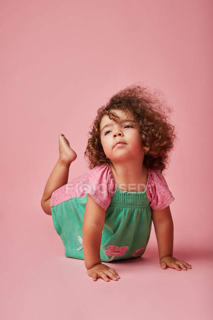 Adorable enfant en bas âge en robe avec les cheveux bouclés regardant loin penché avec les mains sur le sol — Photo de stock