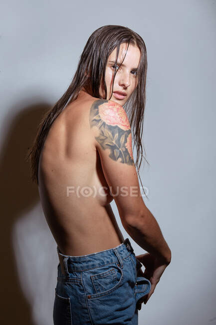 Side view of young female with bare breasts wearing casual jeans standing against gray background — Stock Photo