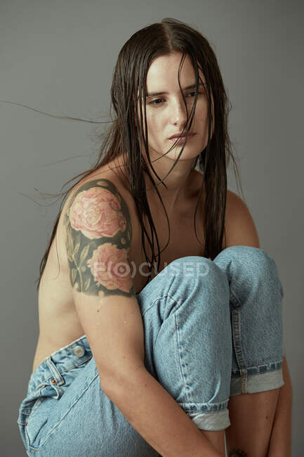 Vista lateral da jovem fêmea com seios nus vestindo jeans casuais em pé contra fundo cinza — Fotografia de Stock