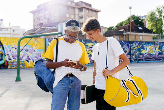 Двоє хлопчиків-підлітків зі скейтбордом та рюкзаком використовують телефон на вулиці — стокове фото