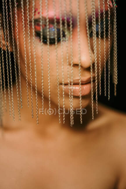Confident ethnic female model wearing headdress with chains with eyes closed on black background in studio — Stock Photo