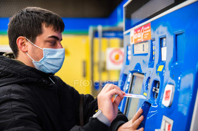 Вид сбоку слепого мужчины в медицинской маске, оплачивающего билет в терминале метро — стоковое фото