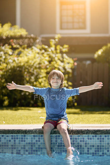 Дитина сидить на краю відкритого басейну і бризкає воду ногами в сонячний літній день — стокове фото