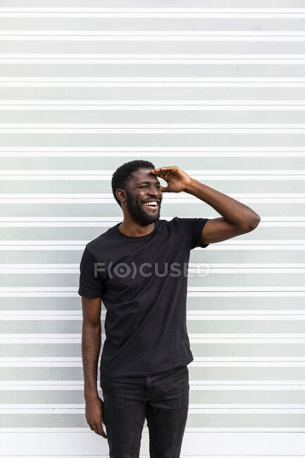 Contenido Hombre afroamericano en camiseta negra de pie mirando a la cámara sobre fondo claro - foto de stock