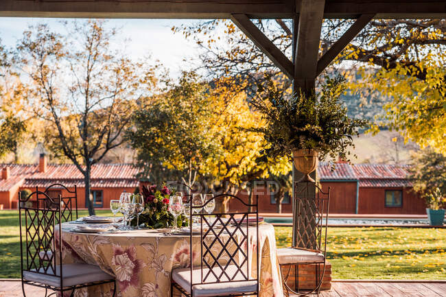 Amplia terraza con platos de viñas y cubiertos colocados en mesas decoradas con flores frescas para la celebración de la boda - foto de stock