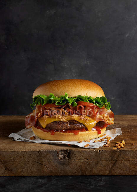 Detail of a delicious burger with cheese and bacon on the wooden table — Stock Photo
