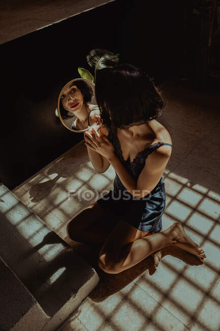Mulher pacífica sentada olhando para si mesma em espelho redondo no chão no quarto — Fotografia de Stock