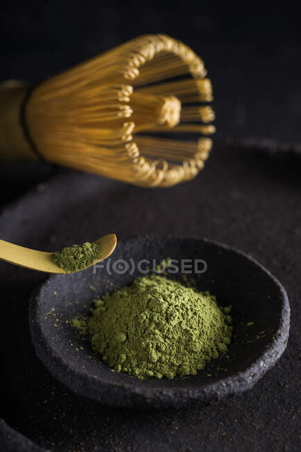 Cuchara con hojas de té matcha secas sobre vajilla negra con chasen para ceremonia oriental tradicional - foto de stock
